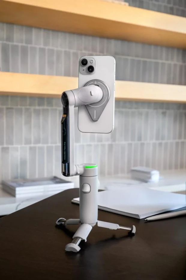 Белый стабилизатор Insta360 Flow Pro на встроенном штативе с вертикально закрепленным iPhone и активным зеленым кольцом светодиодной индикации кругового трекинга