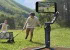Черный стабилизатор DJI Osmo Mobile 6 на комплектном настольном триподе на открытой зеленой поляне на фоне гор удерживает смартфон со сценой бегущих детей
